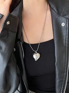 Close-up of a silver heart pendant necklace on a bead chain worn with a leather jacket