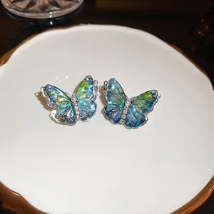 Boucles d'oreilles papillon dégradé bleu avec perles et cristaux sur plateau blanc