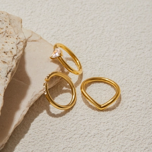 Close-up of three gold stainless steel rings with zircon settings on natural stone
