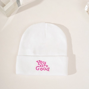 White knitted beanie with pink You are Good embroidery on a minimalist beige surface