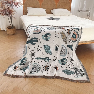 Bohemian woven throw blanket with fringe edge and cactus patterns on a bed