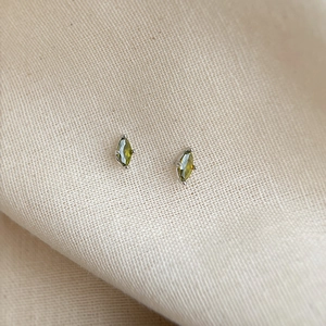 Macro shot of marquise-cut olive green zircon earrings on beige linen fabric