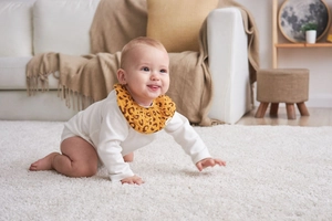 Detailed view of yellow leopard print cotton baby bib with ruffled edge on white romper