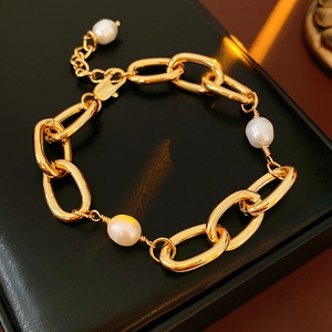 Detail of gold-plated chain bracelet with three freshwater pearls on black leather background