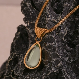 Macro shot of gold plated snake chain with light green waterdrop gemstone on dark rock