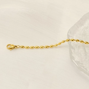 Nahaufnahme der goldenen Edelstahl-Reisperlenkette mit Karabinerverschluss auf Stoff