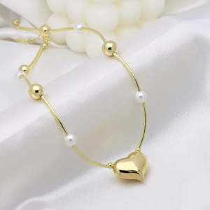 Elegant gold heart pendant bracelet with white pearls on a luxurious white silk backdrop