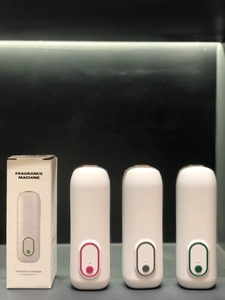 Three smart fragrance dispensers in pink, grey, and green with minimalist wall-mount design