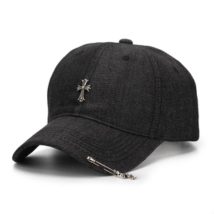 Detailed shot of black denim baseball cap with silver metal cross and punk safety pin