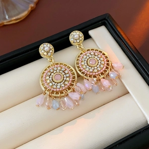 Close-up of golden geometric earrings with pink crystal inlay and beaded fringe tassels