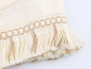 Detail of cream woven fabric featuring gold thread tassels and textured fringe craftsmanship