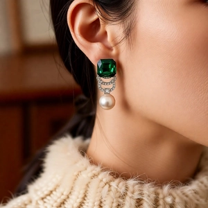 Detail of emerald green gemstone and pearl drop earrings shown on a model