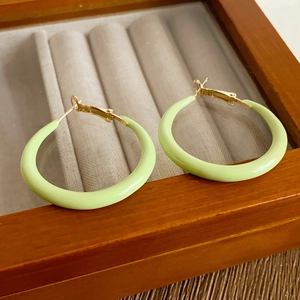 Detailed view of light green drip oil hoop earrings on a vintage wooden jewelry box