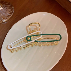 Detail of safety pin hair claw clip with white and green enamel on a ceramic plate