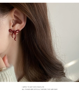 Close-up of a vintage deep red ribbon bow earring worn on ear with white sweater