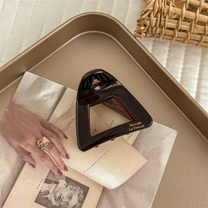 Detailed shot of dark brown acetate hair claw with gold lettering on a vintage tray