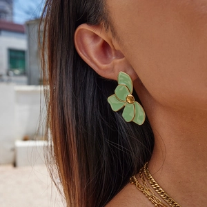Macro shot of green enamel petal earrings with gold trim worn by a model in sunlight