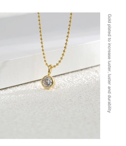 Macro detail of a gold-plated bead chain necklace with a single round zircon pendant