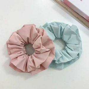 Detail of large matte fabric scrunchies in pastel pink and mint green with layered pleats