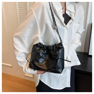 Detail of black leather bucket bag with bow decorations and elegant metal chain strap