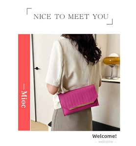 Detail of rose red envelope evening clutch featuring metal trim and gold chain strap