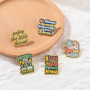 Set of five colorful enamel pins with motivational quotes on a rustic wooden tray