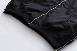 Detail von silbernem Metallreißverschluss und schwarzem Rippbündchen an einer Bomberjacke