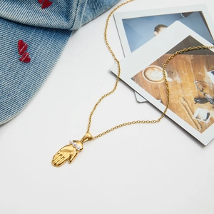 Détail du pendentif main en or 18k avec perles sur chaîne vintage et fond en jean