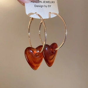 Macro shot of gold hoop earrings with translucent amber acrylic heart charms