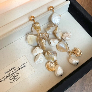 Detailed close-up of shell tassel earrings in a beige velvet jewelry box with golden accents