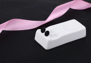 Detailed close-up of S925 silver round black crystal stud earrings on white ceramic base