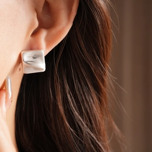 Close-up of square silver earrings with irregular lava texture worn by a model