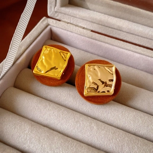 Macro shot of gold square textured earrings with brown flocked backing in a jewelry box
