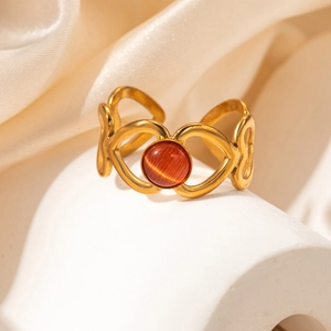 Gros plan d'une bague coeur dorée ajourée avec pierre oeil de chat rouge orangé
