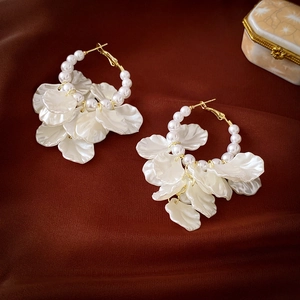 Elegant white petal and pearl hoop earrings with gold metal accents on red fabric