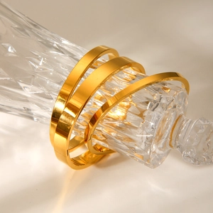Three-piece set of minimalist gold-plated stainless steel bangles on a crystal glass bottle