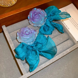 Détail d'un nœud en satin bleu et pétales de rose en résine pailletée sur une boucle
