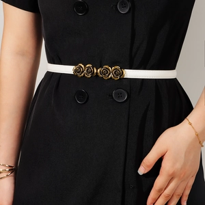 Detail of white thin belt featuring a golden rose-shaped metal buckle on a black dress