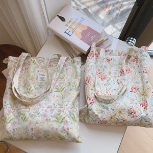 Détail de deux sacs cabas en toile fleurie rose et orange posés sur une table blanche