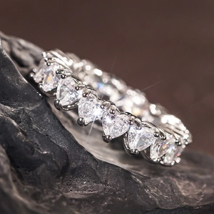 Macro shot of heart-cut cubic zirconia stones set in a silver eternity ring on dark stone