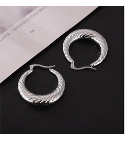 Macro shot of silver twisted hoop earrings with textured finish on leather and magazine