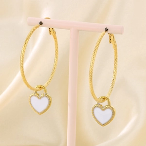 Detail of gold heart earrings with white enamel on a soft beige silk background