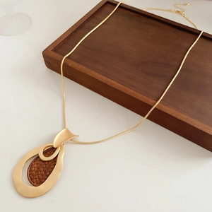 Detailed view of bohemian teardrop wood pendant necklace with gold chain on wooden tray