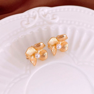 Detail of vintage golden flower earrings with pearl centers on a white ceramic plate