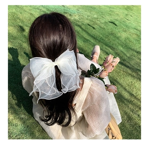 Close-up of a large white organza bow hair clip worn by a model in a natural grass setting
