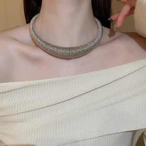 Close-up of a silver chunky metal torque necklace with textured details on a model