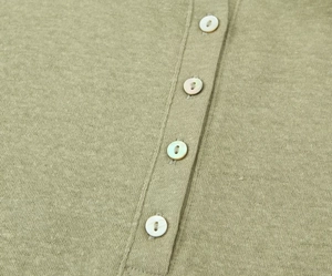 Detail of light olive green knit tee featuring decorative white buttons and fine texture