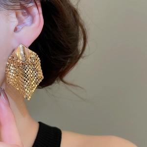 Close-up of golden rhombus sequin tassel earrings worn by a model in soft lighting