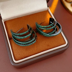 Macro shot of multi-layer C-shaped earrings with green zircons in a brown jewelry box