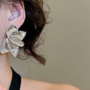 Macro detail of silver leaf-shaped earrings with textured surface on female model